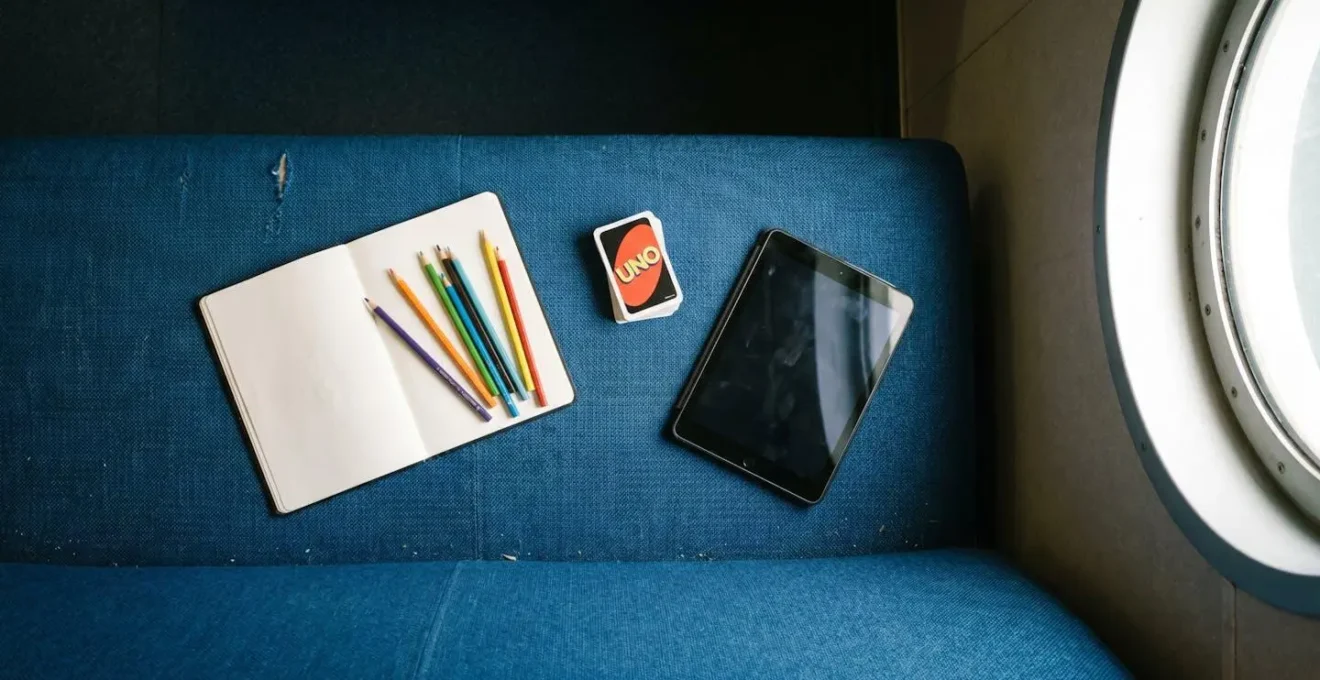 Contenu d'un sac d'activités pour enfant posé sur un siège de ferry : carnet de dessin, jeu de cartes, tablette